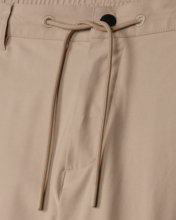 Close-up image of the MENS LLOYD CARGO JOGGER - B6P159B200 by Psycho Bunny, showcasing the beige jogger pants with a black button at the waistband, an elastic drawstring with orange and white stripes for tightening, and a side pocket. The fabric appears smooth and slightly matte, exuding subtle embroidery refinement.