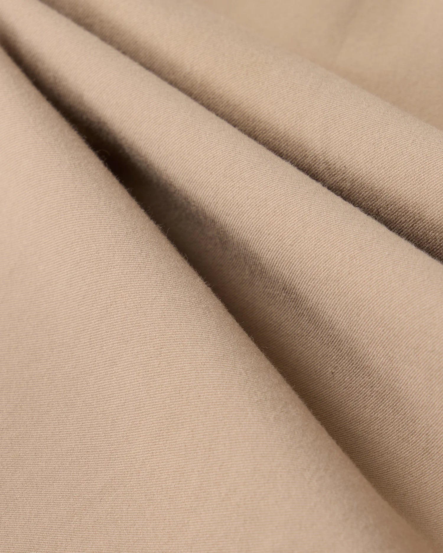 Close-up of beige fabric with a soft, smooth texture and subtle folds. The material appears lightweight and finely woven, suggesting it could be used for clothing or upholstery. The color and texture give a cozy and comfortable impression, making it perfect for the Psycho Bunny MENS LLOYD CARGO JOGGER - B6P159B200's snap fastening pockets.