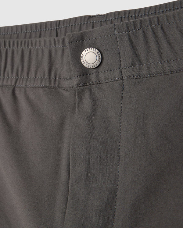Close-up of the waistband of a pair of dark green MENS MADISON COMMUTER PANT - B6P395Z1WB by Psycho Bunny. The waistband features an elastic section and a fastening silver button engraved with "PATAGONIA" and "since 1973." The stitching and material are clearly visible, along with subtle Psycho Bunny detailing.
