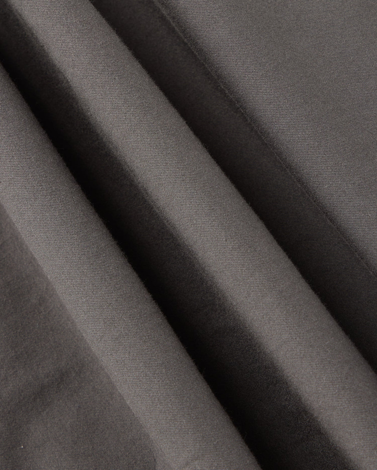 Close-up of smooth, dark grey fabric with soft wrinkles and folds, showcasing the fine texture and matte finish. This material, part of the MENS MADISON COMMUTER PANT - B6P395Z1WB by Psycho Bunny, creates a sense of depth and shadow throughout the image. Look closely to find subtle bunny detailing that adds a unique touch.