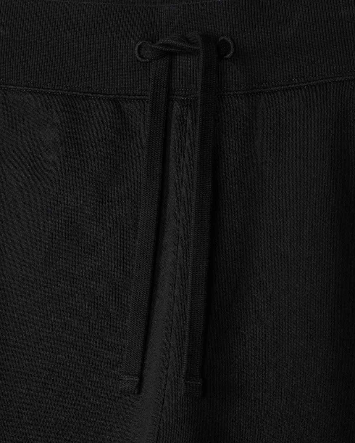 Close-up of the MENS LEVY ESSENTIAL FLEECE SWEATPANT - B6P721D200 by Psycho Bunny, showcasing black cotton sweatpants with an elastic waistband. The waistband features a matching black drawstring tied in a simple bow at the center. The texture of the fabric is visible, indicating comfort and durability, making them perfect for casual wear.
