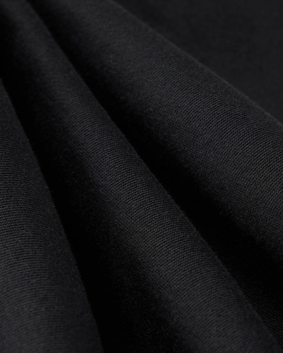 Close-up image of the MENS LEVY ESSENTIAL FLEECE SWEATPANT - B6P721D200 by Psycho Bunny in black fabric, highlighting its smooth texture and soft folds. The tightly woven material with a slight sheen suggests it is perfect for high-quality cotton sweatpants.