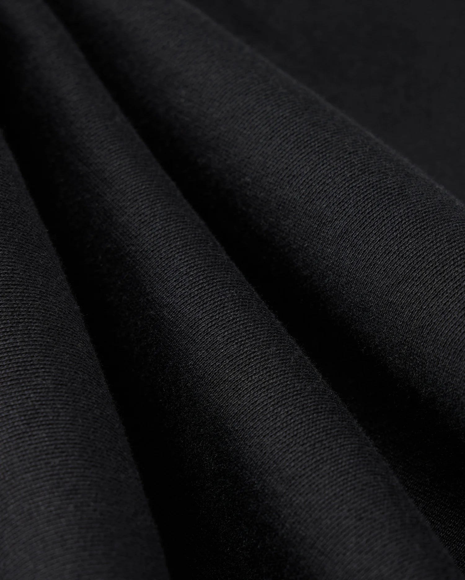 Close-up image of the MENS LEVY ESSENTIAL FLEECE SWEATPANT - B6P721D200 by Psycho Bunny in black fabric, highlighting its smooth texture and soft folds. The tightly woven material with a slight sheen suggests it is perfect for high-quality cotton sweatpants.
