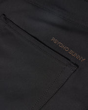 The MENS MAVERICK 10K PANT - B6P788D200 from Psycho Bunny showcases a sleek pocket in a close-up of the dark fabric. The brand name "PSYCHO BUNNY" is embroidered in a contrasting color near the edge, enhancing its modern design with four-way stretch for ultimate comfort.