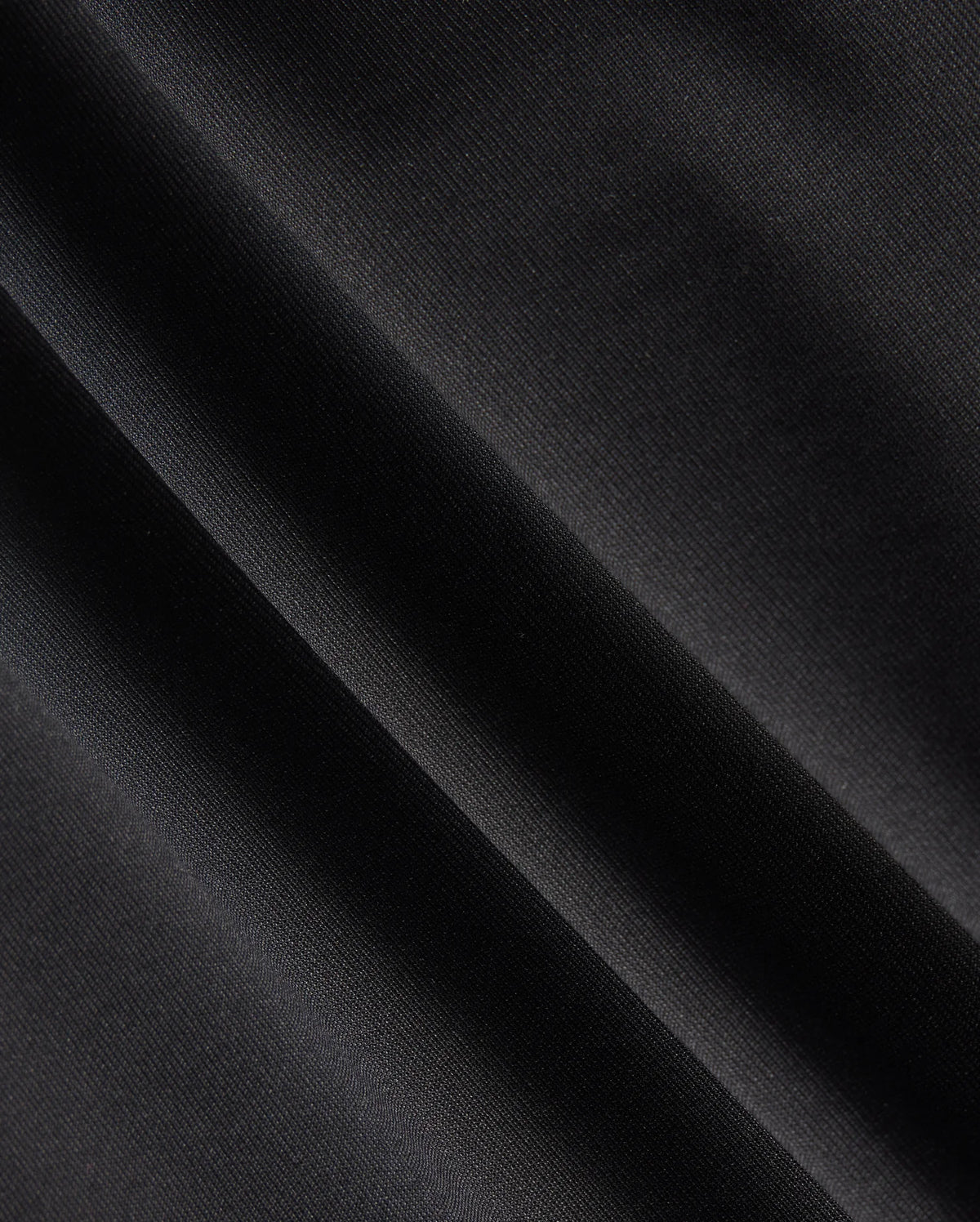 Close-up of a dark fabric with diagonal folds, showcasing a smooth texture and subtle sheen under light, reminiscent of the material in the Psycho Bunny MENS MAVERICK 10K PANT - B6P788D200. The fabric appears to be made of a fine, tightly woven material with impressive four-way stretch capabilities.