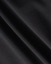 Close-up of a dark fabric with diagonal folds, showcasing a smooth texture and subtle sheen under light, reminiscent of the material in the Psycho Bunny MENS MAVERICK 10K PANT - B6P788D200. The fabric appears to be made of a fine, tightly woven material with impressive four-way stretch capabilities.