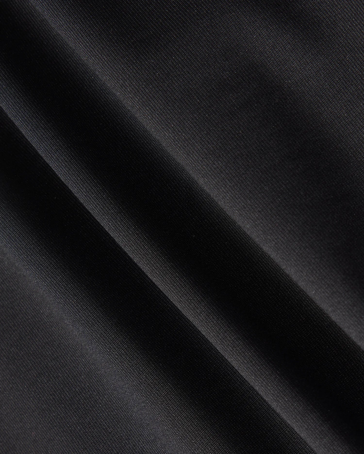 Close-up of a dark fabric with diagonal folds, showcasing a smooth texture and subtle sheen under light, reminiscent of the material in the Psycho Bunny MENS MAVERICK 10K PANT - B6P788D200. The fabric appears to be made of a fine, tightly woven material with impressive four-way stretch capabilities.
