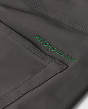 Close-up of gray fabric with visible stitching and a green "Psycho Bunny" embroidered logo on the MENS MAVERICK 10K PANT - B6P788D200, featuring five practical pockets for everyday ease.