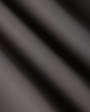 Close-up of the smooth, dark grey fabric of the Psycho Bunny MENS MAVERICK 10K PANT - B6P788D200 showcases subtle diagonal ripples and a matte finish. The folds create gentle shadows, highlighting its texture, slight sheen, and five-pocket practicality.