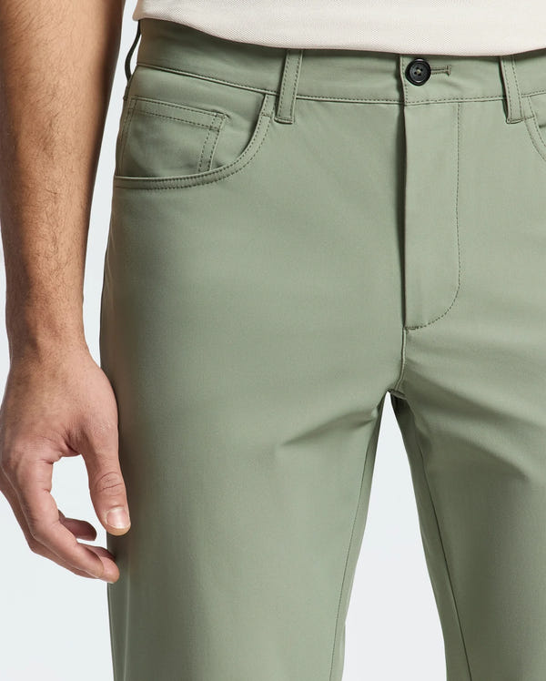 A person in Psycho Bunny's Men's Maverick 10K Step Pants, light green, with one hand partially visible on a crisp white background. These pants feature a button and zipper closure, handy front pockets, and a stylish design with four-way stretch fabric.