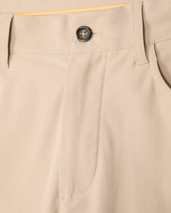 Close-up of the beige Psycho Bunny MENS MAVERICK 10K PANT - B6P788D200 showcasing a waistband with belt loops, a dark button, and a front pocket. The fabric appears smooth and is neatly stitched, offering four-way stretch for comfort. The stitching and design provide a casual yet tailored look.