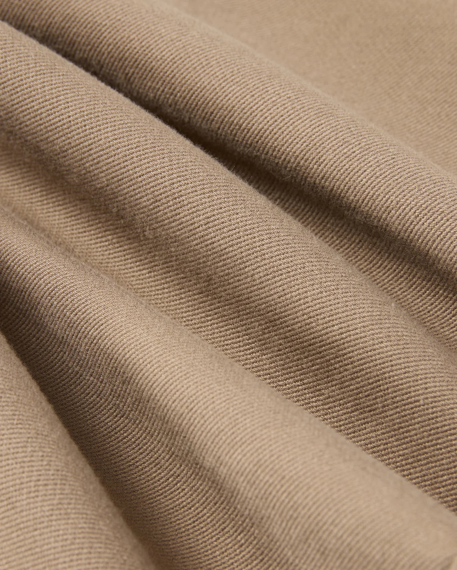 Close-up of the light brown twill fabric from the MENS HAYS TWILL PANT (B6P894D200) by Psycho Bunny, featuring a diagonal weave pattern. The material is slightly draped to highlight its texture and soft folds, offering ultimate comfort.