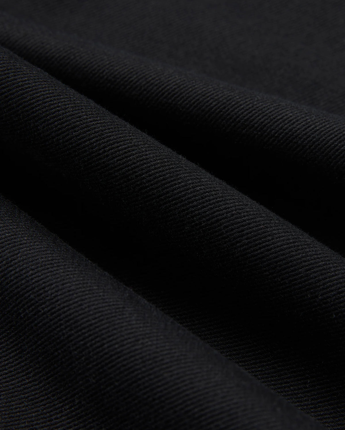 Close-up of the black cotton-blend twill fabric used in the MENS HAYS TWILL PANT - B6P894D200 by Psycho Bunny, featuring diagonal lines that highlight its textured surface and smooth folds. The material appears thick and finely woven, providing ultimate comfort while subtly reflecting light.
