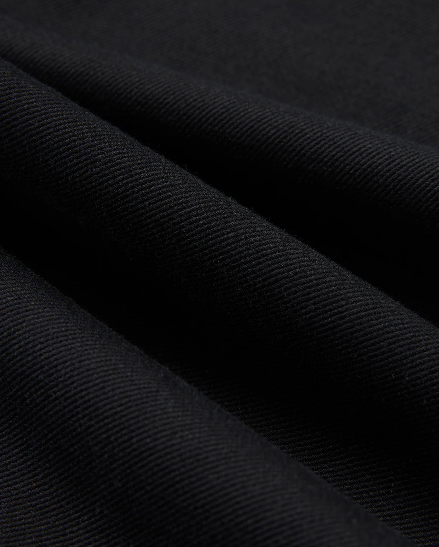 Close-up of the black cotton-blend twill fabric used in the MENS HAYS TWILL PANT - B6P894D200 by Psycho Bunny, featuring diagonal lines that highlight its textured surface and smooth folds. The material appears thick and finely woven, providing ultimate comfort while subtly reflecting light.