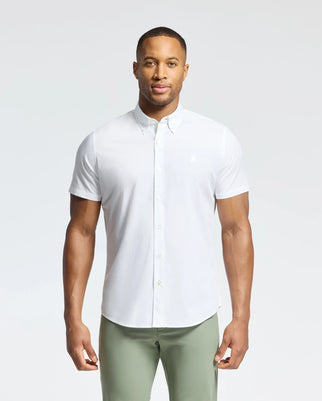 A person faces forward wearing a Psycho Bunny MENS GABRIEL SHORT SLEEVE SHIRT in white, crafted from soft Pima cotton, paired with light green pants against a plain white background.