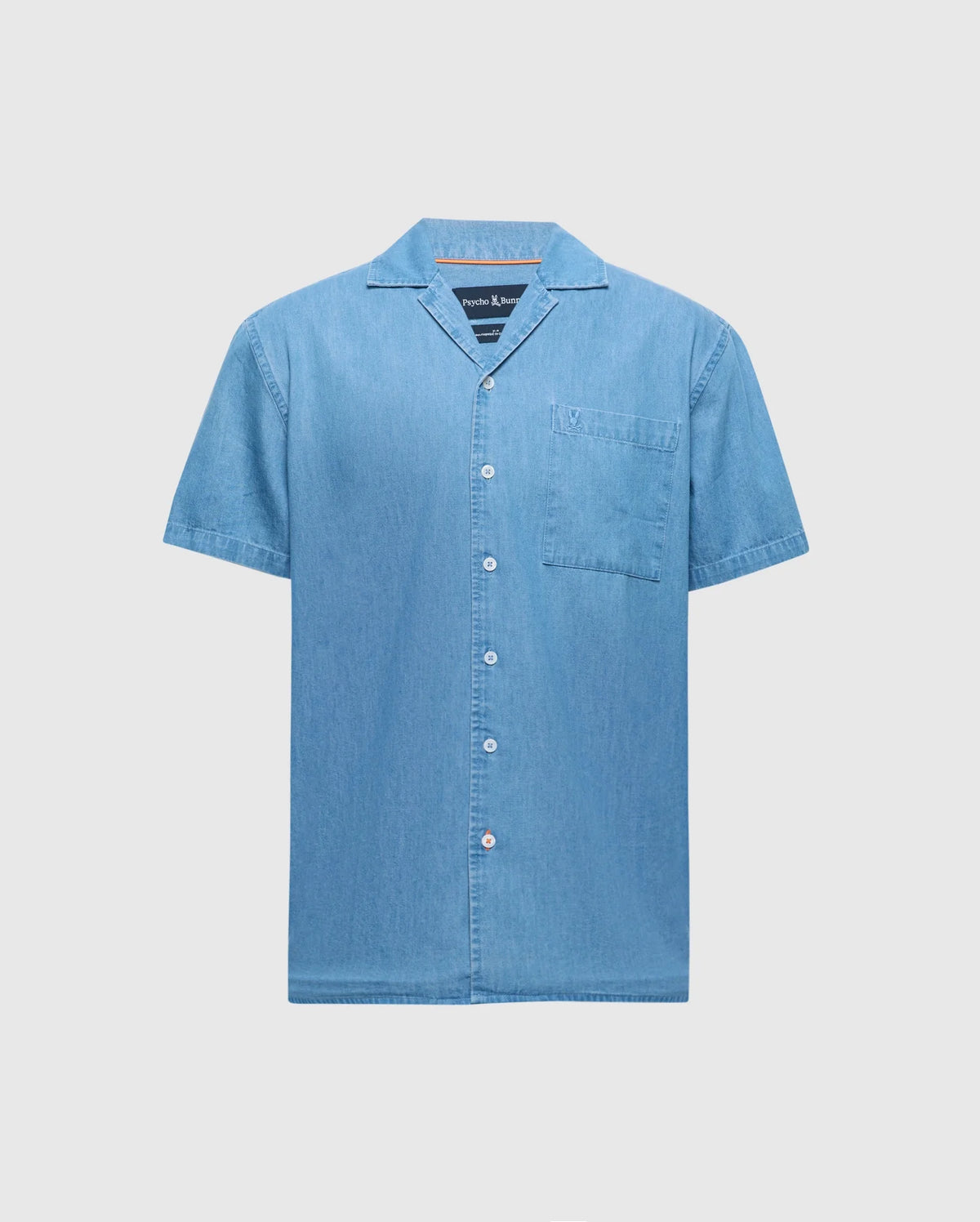 The Psycho Bunny MENS KERVIN LIGHTWEIGHT DENIM WOVEN SHIRT (B6Q467F200) features short sleeves, a light blue hue, luxe finishes, a button-down front, and a chest pocket, set against a plain white background.