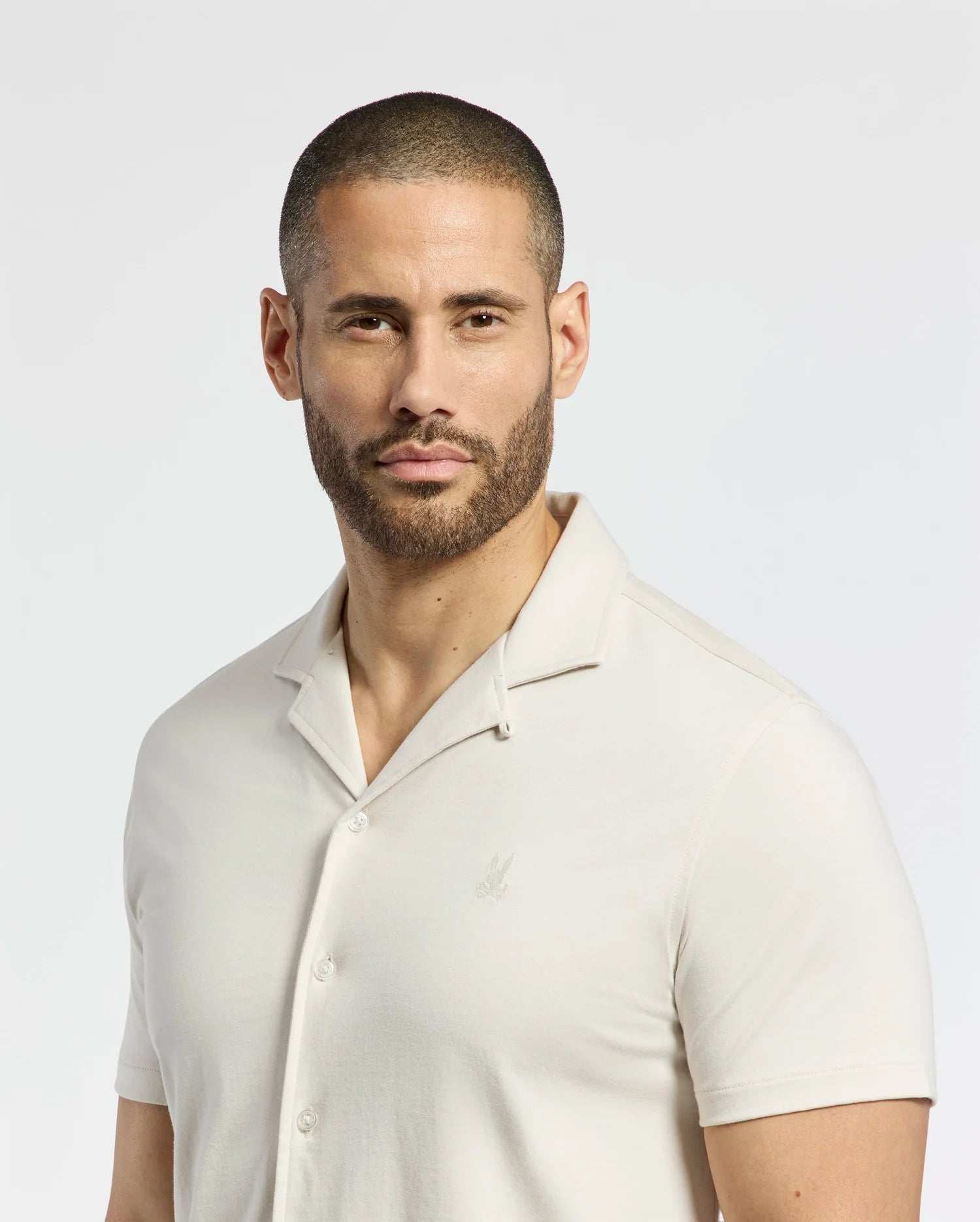 A man with a shaved head and beard wears the Psycho Bunny MENS BRYAN CAMP COLLAR SHORT SLEEVE SHIRT - B6Q581F200 made of performance fabric, against a plain white background.