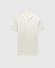The Psycho Bunny MENS BRYAN CAMP COLLAR SHORT SLEEVE SHIRT - B6Q581F200, in light beige, features a classic collar and white buttons. Crafted from a Pima Cotton Blend, this shirt offers a soft feel for ultimate comfort and is displayed against a gray background highlighting its clean design.