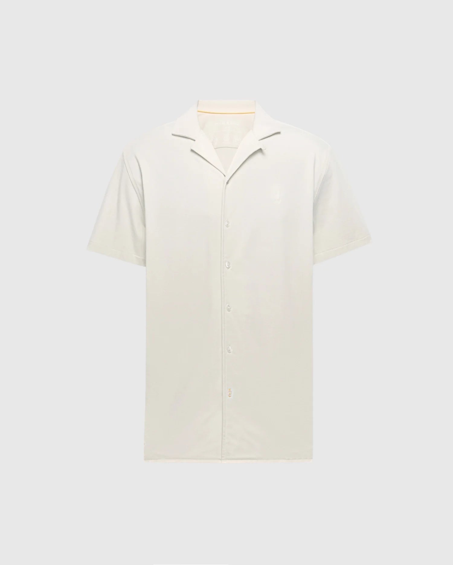 The Psycho Bunny MENS BRYAN CAMP COLLAR SHORT SLEEVE SHIRT - B6Q581F200, in light beige, features a classic collar and white buttons. Crafted from a Pima Cotton Blend, this shirt offers a soft feel for ultimate comfort and is displayed against a gray background highlighting its clean design.