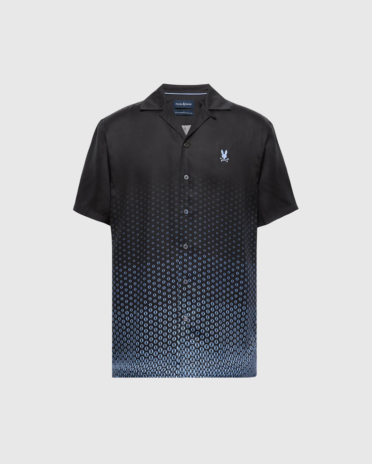 Psycho Bunny's MENS BENDIGO TENCEL SHIRT - B6Q627F200 is a short-sleeve black button-up with a blue ombre dot pattern at the bottom. Made from soft Tencel, it features a camp collar for a casual look and has a small emblem on the left chest.
