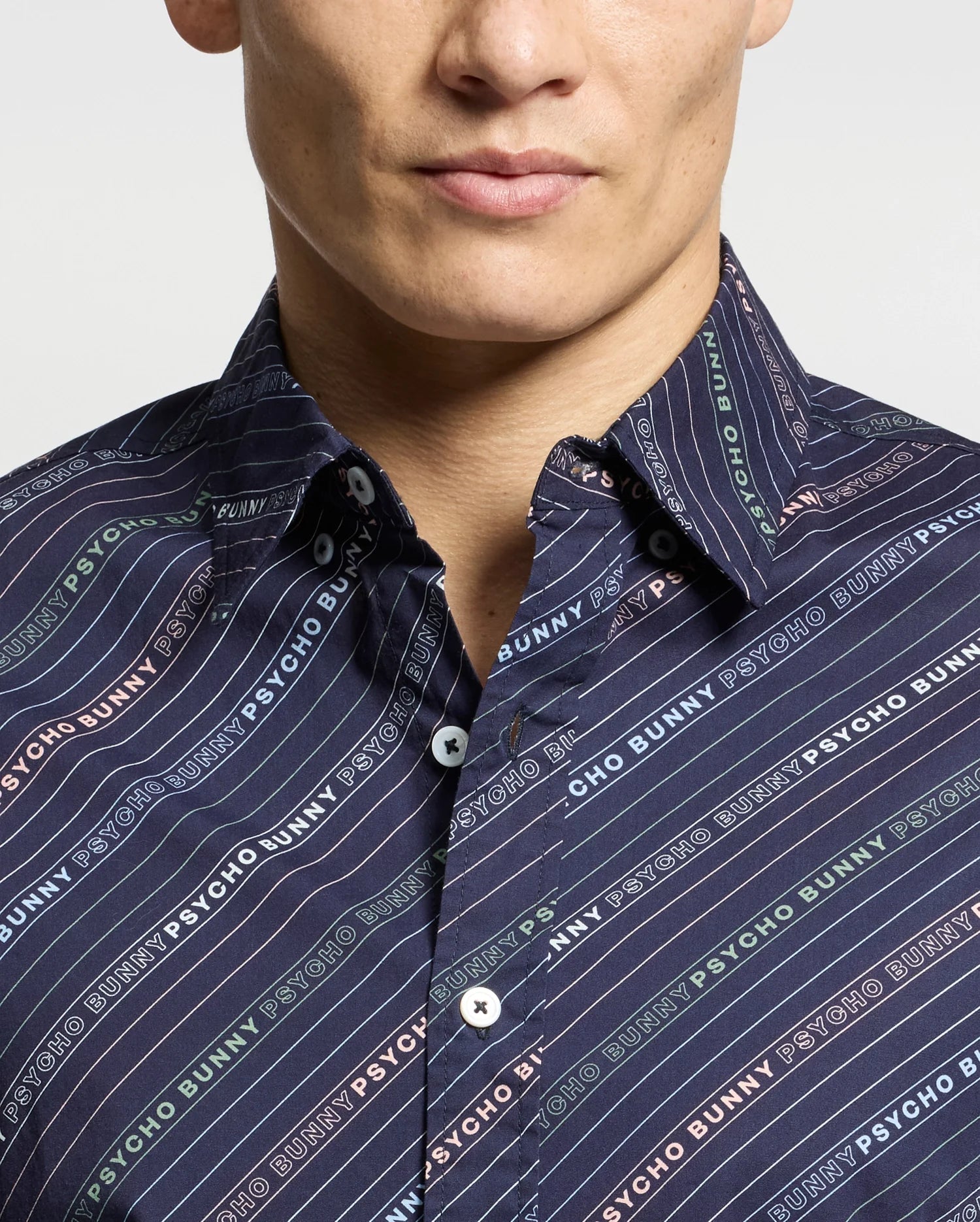 A person sports the MENS RENMARK STRETCH POPLIN WOVEN SHIRT by Psycho Bunny, showcasing a colorful logo-striped pattern. Crafted from stretch poplin for comfort, it features white buttons and a partially visible face among the vibrant stripes.