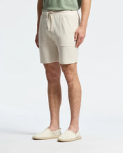 A person effortlessly radiates casual-chic style in Psycho Bunny's MENS TAYLOR LIGHT PIQUE SWEATSHORT - B6R344F200, featuring a drawstring and front pockets, teamed with espadrilles and a light green shirt against a plain white backdrop.