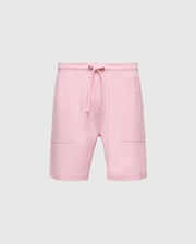 The MENS TAYLOR LIGHT PIQUE SWEATSHORT - B6R344F200 by Psycho Bunny pairs pink shorts with a drawstring waistband against a gray background. Made from lightweight Pima cotton, they offer knee-length style, side pockets, and casual-chic appeal for everyday wear.