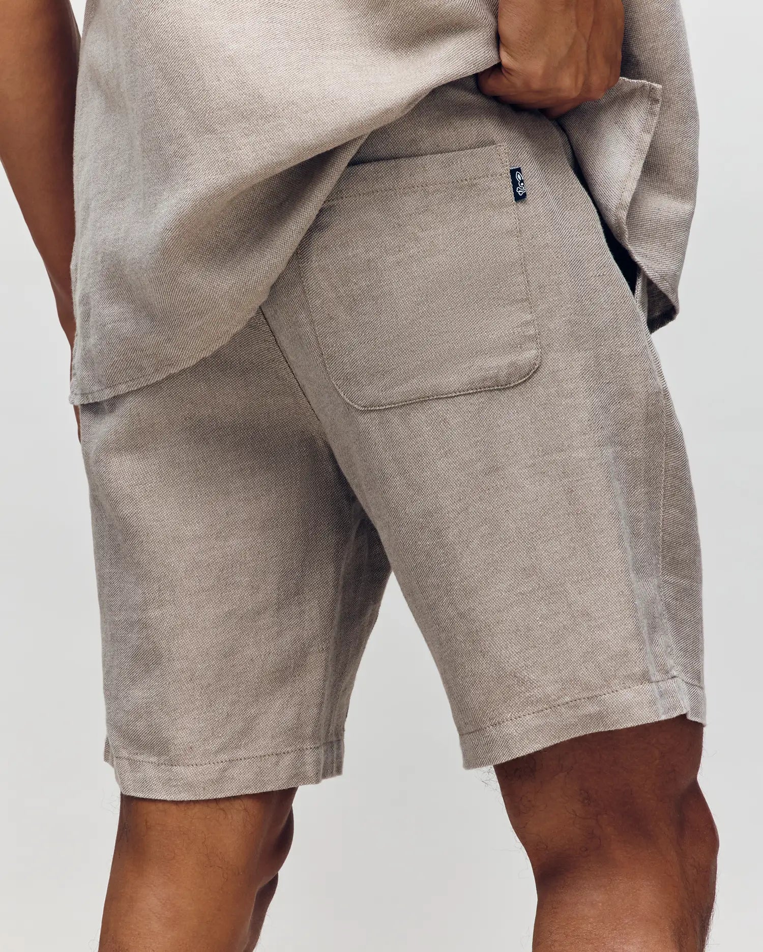 Wearing Psycho Bunny's MENS WINDCREST LINEN BLEND DRAWSTRING SHORT - B6R474C200, a person poses with one hand on their hip, highlighting the textured fabric and back pocket for an effortless summer style.