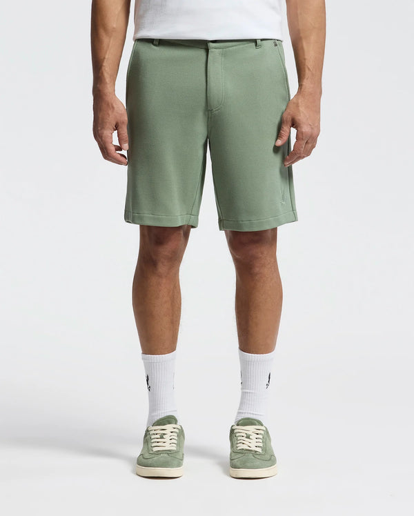 A person wears the Psycho Bunny MENS SHIRO KNIT HONEYCOMB SHORT - B6R585F200, paired with piqué sneakers and crisp white socks against a plain white background, showcasing just their lower half.
