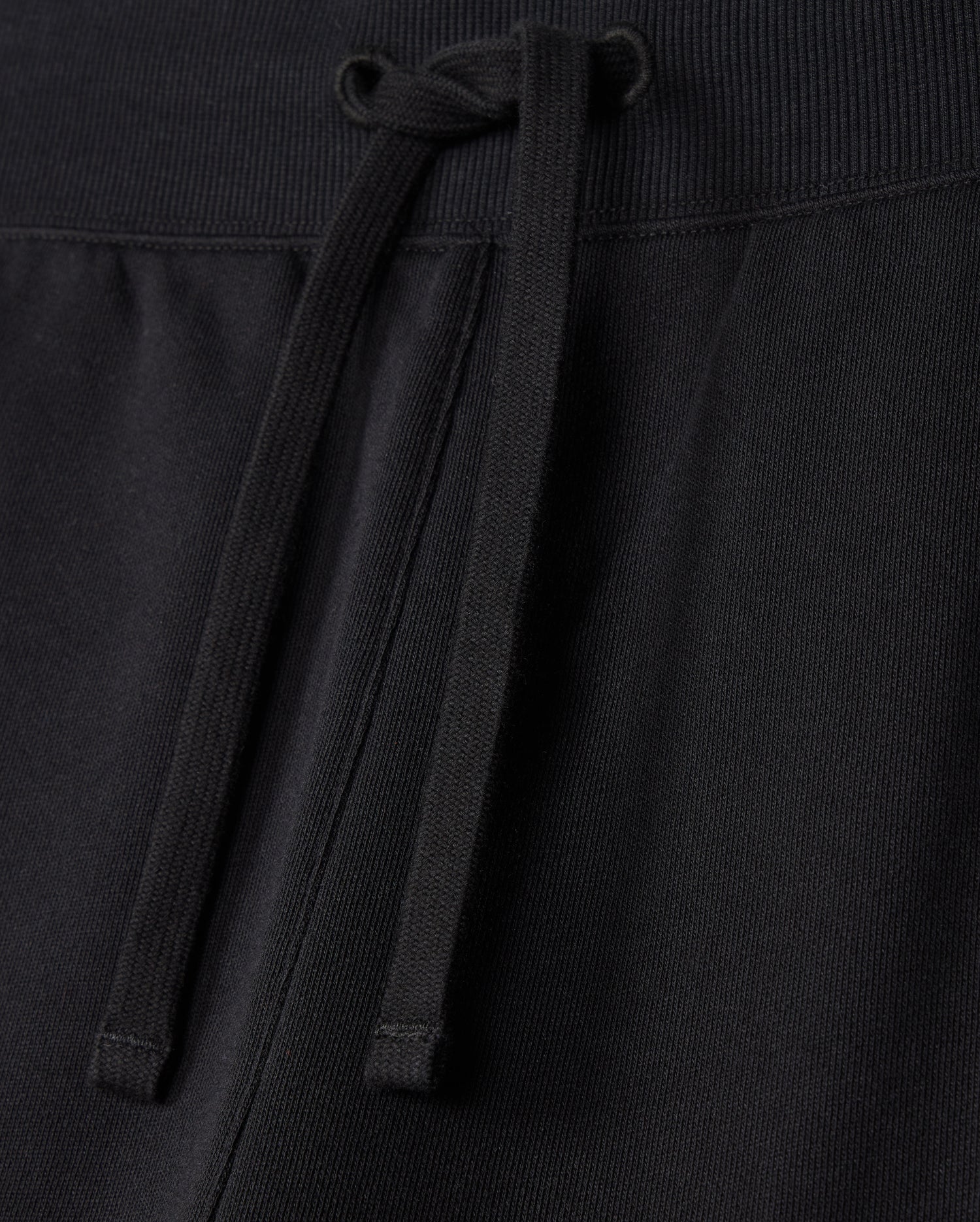 Close-up image of MENS LEVY FLEECE SWEATSHORT - B6R862D200 by Psycho Bunny, showcasing a black sweatshort with a drawstring waistband. The cozy french terry fabric texture is visible, emphasizing the casual and regular fit design. The strings are tied loosely in the center.