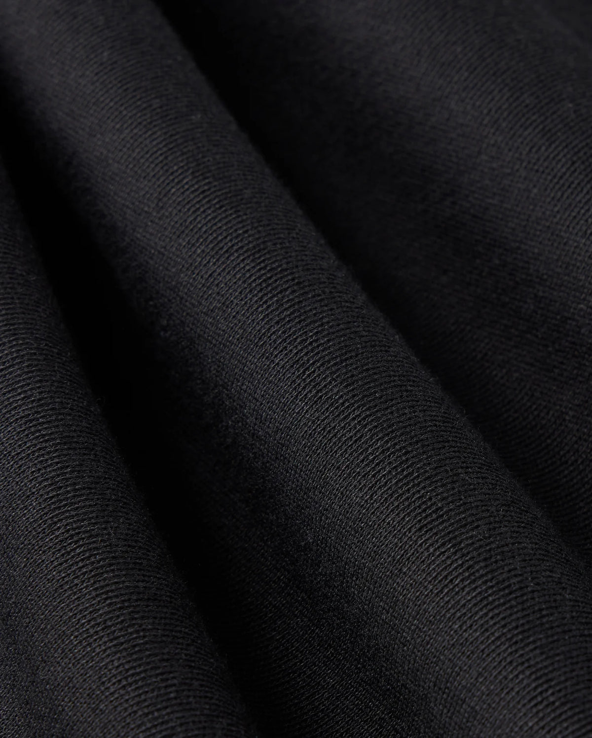 Close-up of the black French terry fabric from the MENS LEVY FLEECE SWEATSHORT - B6R862D200 by Psycho Bunny, showcasing its visible texture. The smooth, velvety surface of the fabric is draped in gentle folds, with lighting that highlights the subtle differences in texture and shading.