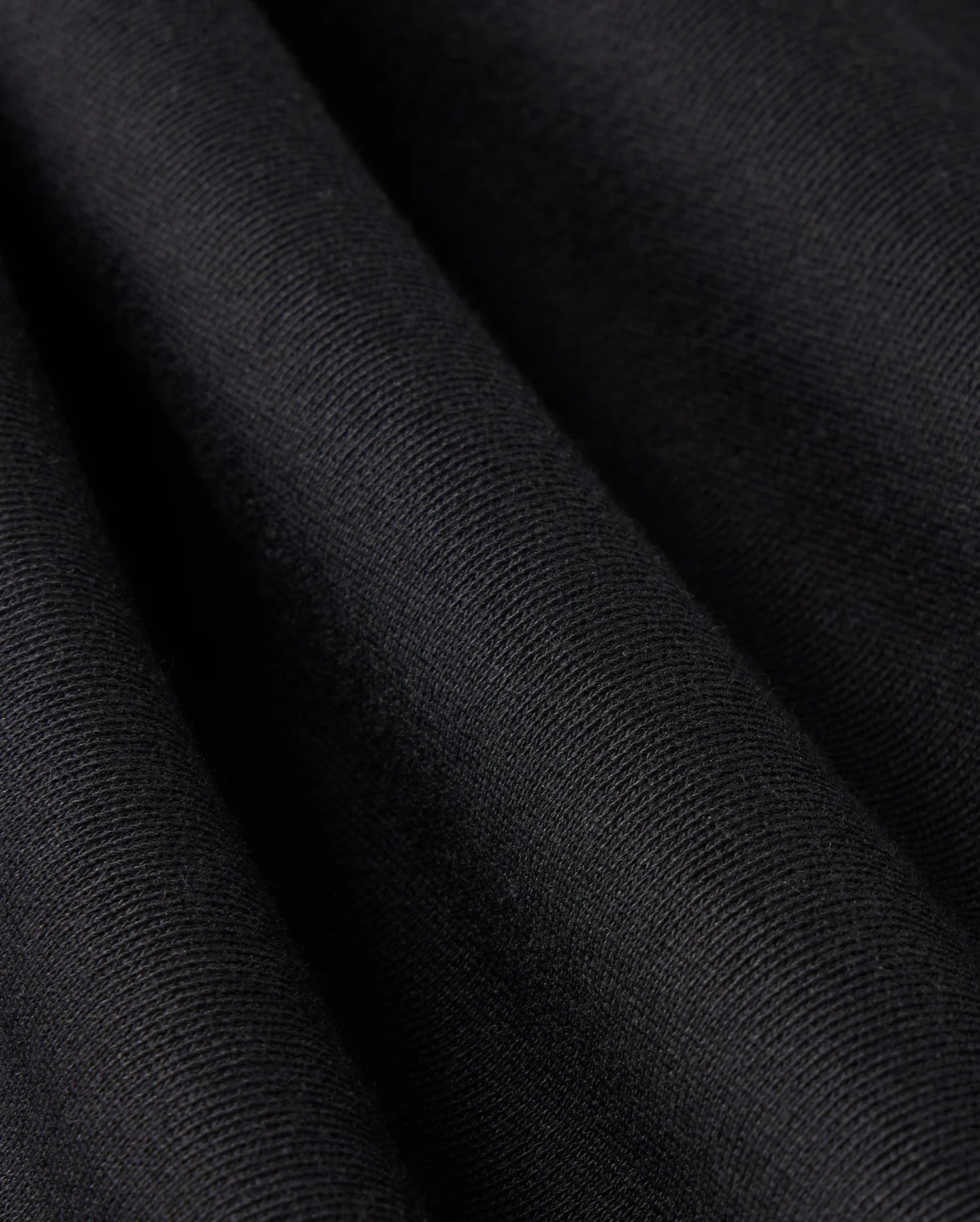 Close-up of the black French terry fabric from the MENS LEVY FLEECE SWEATSHORT - B6R862D200 by Psycho Bunny, showcasing its visible texture. The smooth, velvety surface of the fabric is draped in gentle folds, with lighting that highlights the subtle differences in texture and shading.
