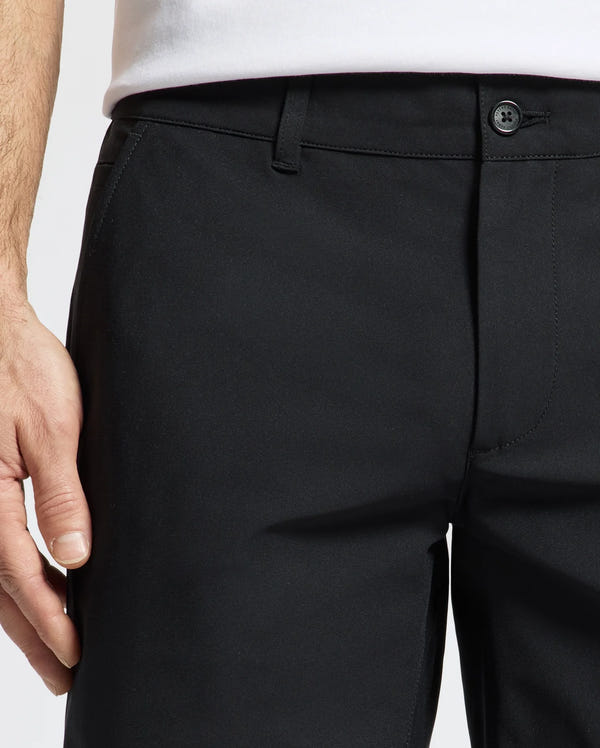 Close-up of a person in Psycho Bunny's MENS 10K STEP SHORT - B6R969F200, paired with a white shirt. Designed for athletic breathability, it ensures comfort as the person's left hand rests casually near the pocket.