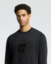 A man wearing the MENS OAK CITY CREW NECK - B6S274E200 by Psycho Bunny, featuring a premium quality design with a rectangular pattern and subtle raised embroidery logo on the front, stands against a light grey background.