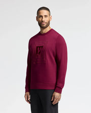 Against a white backdrop, a man models the Psycho Bunny MENS OAK CITY CREW NECK - B6S274E200 in maroon. Featuring subtle chest embroidery, his short hair and beard complement the sweater's stylish yet understated appeal.