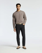 Against a plain background, someone wears the MENS PIERCE PEACHED TERRY CREW - B6S278E200 taupe sweatshirt by Psycho Bunny. Paired with black pants, a beige belt, and brown loafers, their effortlessly stylish look includes relaxed hands by their sides as they gaze ahead.