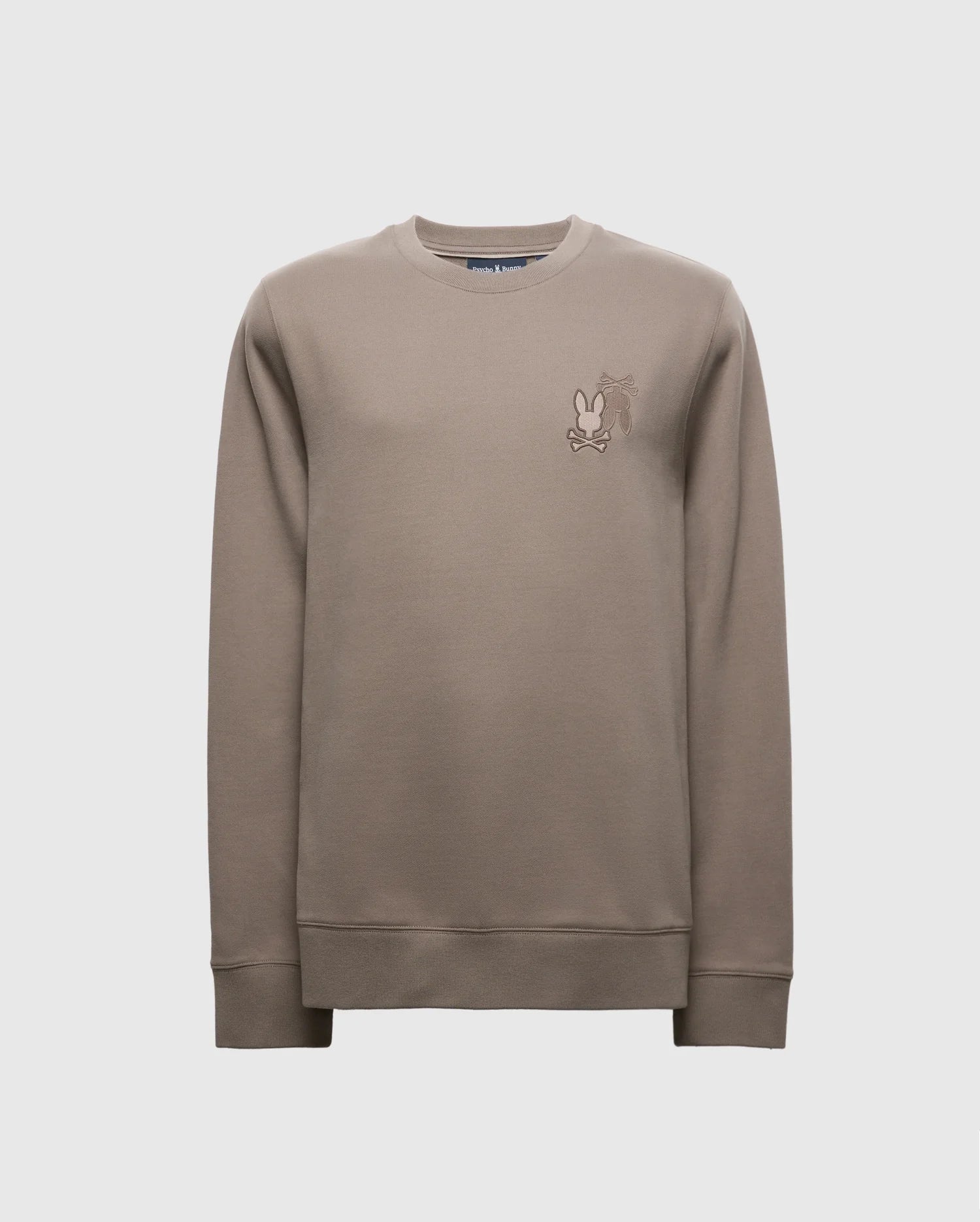The Psycho Bunny MENS PIERCE PEACHED TERRY CREW - B6S278E200 is a stylish beige sweater made from premium cotton. It features an embroidered cartoon character on the chest and includes a classic crew neck with ribbed cuffs and hem, all set against a plain white background.