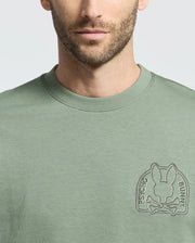 A person wearing the Psycho Bunny Men's Melbourne Embroidered Classic Modal Crewneck Sweatshirt, featuring a stylized bunny above crossed bones with "Psycho Bunny" text in a circular logo on the chest, all embossed in a slightly lighter green on soft stretch jersey fabric.