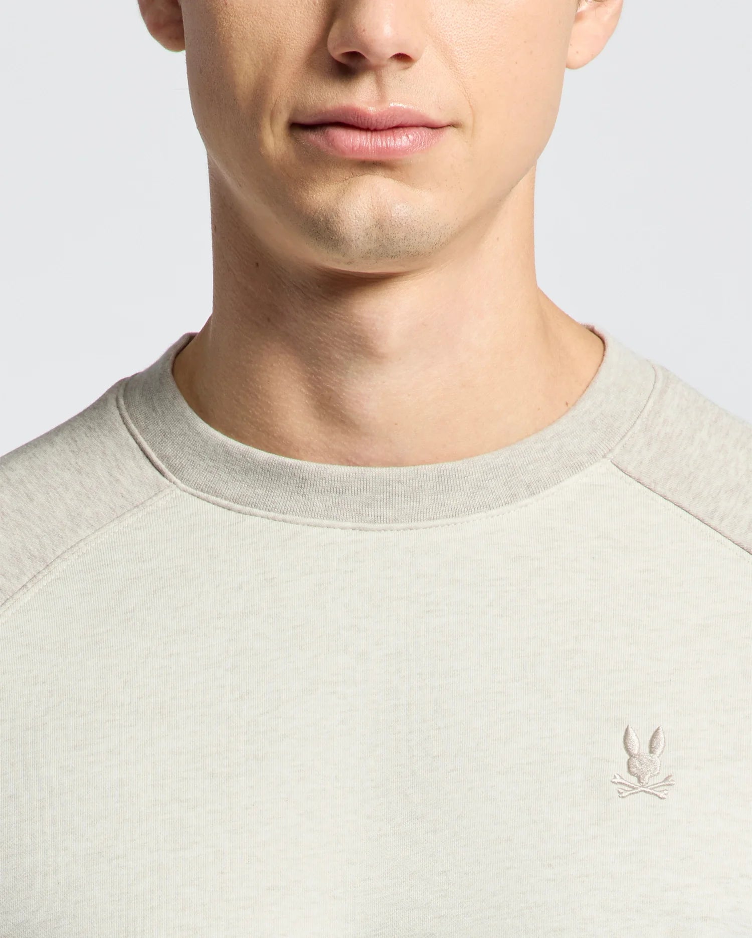 The Psycho Bunny MENS ARCHIE MELANGE COLOR BLOCK SWEATSHIRT - B6S630F200, crafted from soft cotton jersey, features an embroidered bunny with crossed golf clubs on the chest. A neutral backdrop enhances its monochrome style and subtle details.