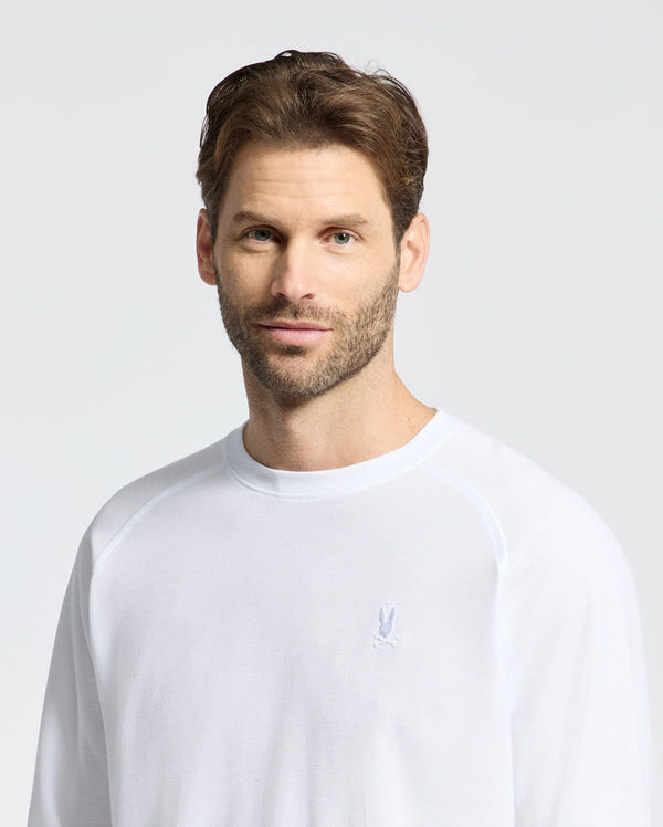 A person with short brown hair and a beard is wearing the Psycho Bunny MENS TAYLOR PIQUE LONG SLEEVE TEE - B6T580F200, featuring an embroidered bunny on the chest, against a neutral background.