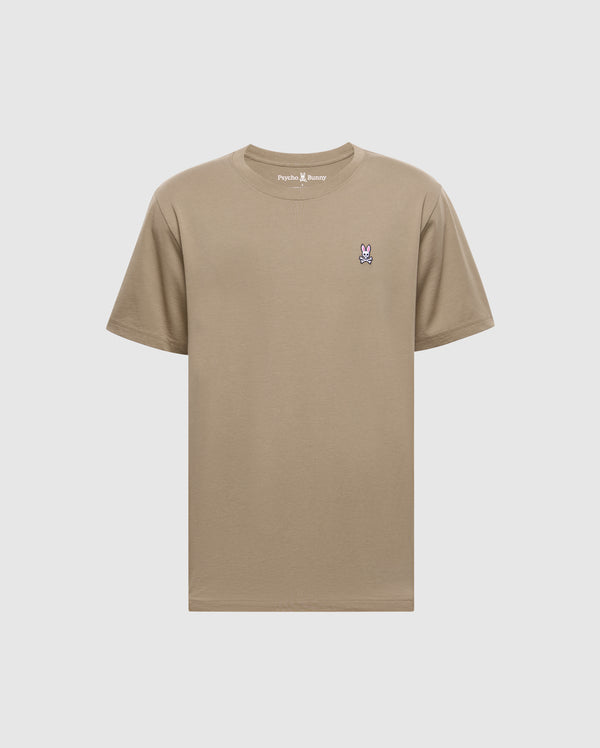 The Psycho Bunny Men's Classic Crew Neck Tee (B6U014CRPC) is a beige short-sleeve shirt with a pink and purple rabbit logo on the left chest. Made from 100% Pima cotton, it features taped seams and the "Psycho Bunny" brand name at the neckline against a plain background.