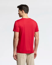 A person stands facing away, wearing a classic red Psycho Bunny MENS CLASSIC CREW NECK TEE - B6U014CRPC and light beige pants against a plain white background.