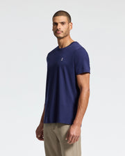 A man stands against a plain white background wearing a Psycho Bunny MENS CLASSIC CREW NECK TEE, B6U014CRPC, in navy blue. The regular fit tee features a small embroidered logo on the chest and is crafted from soft pima cotton. It perfectly complements his beige pants as he looks forward neutrally.