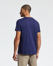 A man wearing a Psycho Bunny MENS CLASSIC CREW NECK TEE - B6U014CRPC in navy blue and beige pants stands with his back to the camera against a plain white background.