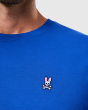 A person wearing the MENS CLASSIC CREW NECK TEE - B6U014CRPC by Psycho Bunny, crafted from soft Pima cotton and featuring an embroidered Bunny logo with a skull and crossbones design complete with rabbit ears.