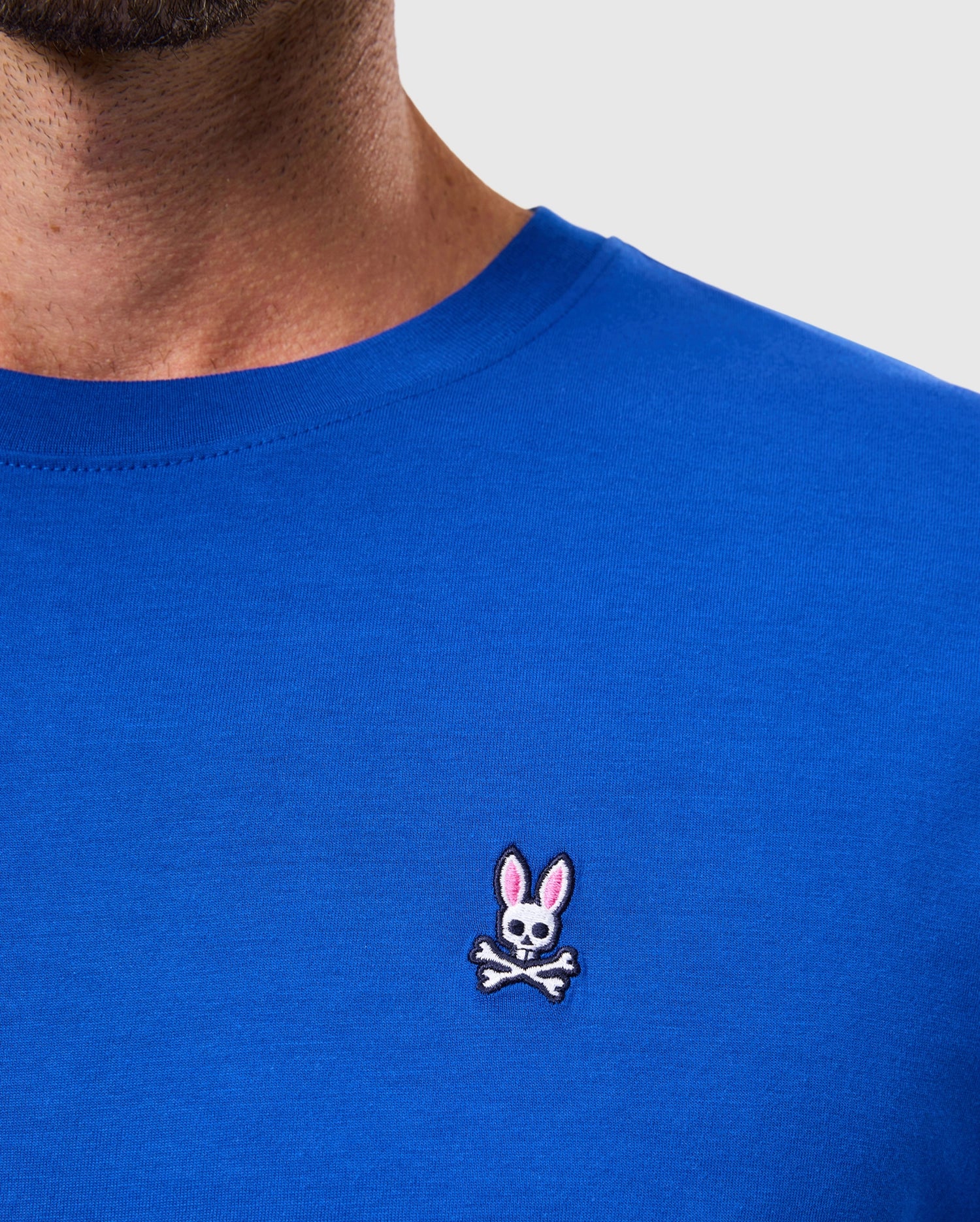 A person wearing the MENS CLASSIC CREW NECK TEE - B6U014CRPC by Psycho Bunny, crafted from soft Pima cotton and featuring an embroidered Bunny logo with a skull and crossbones design complete with rabbit ears.