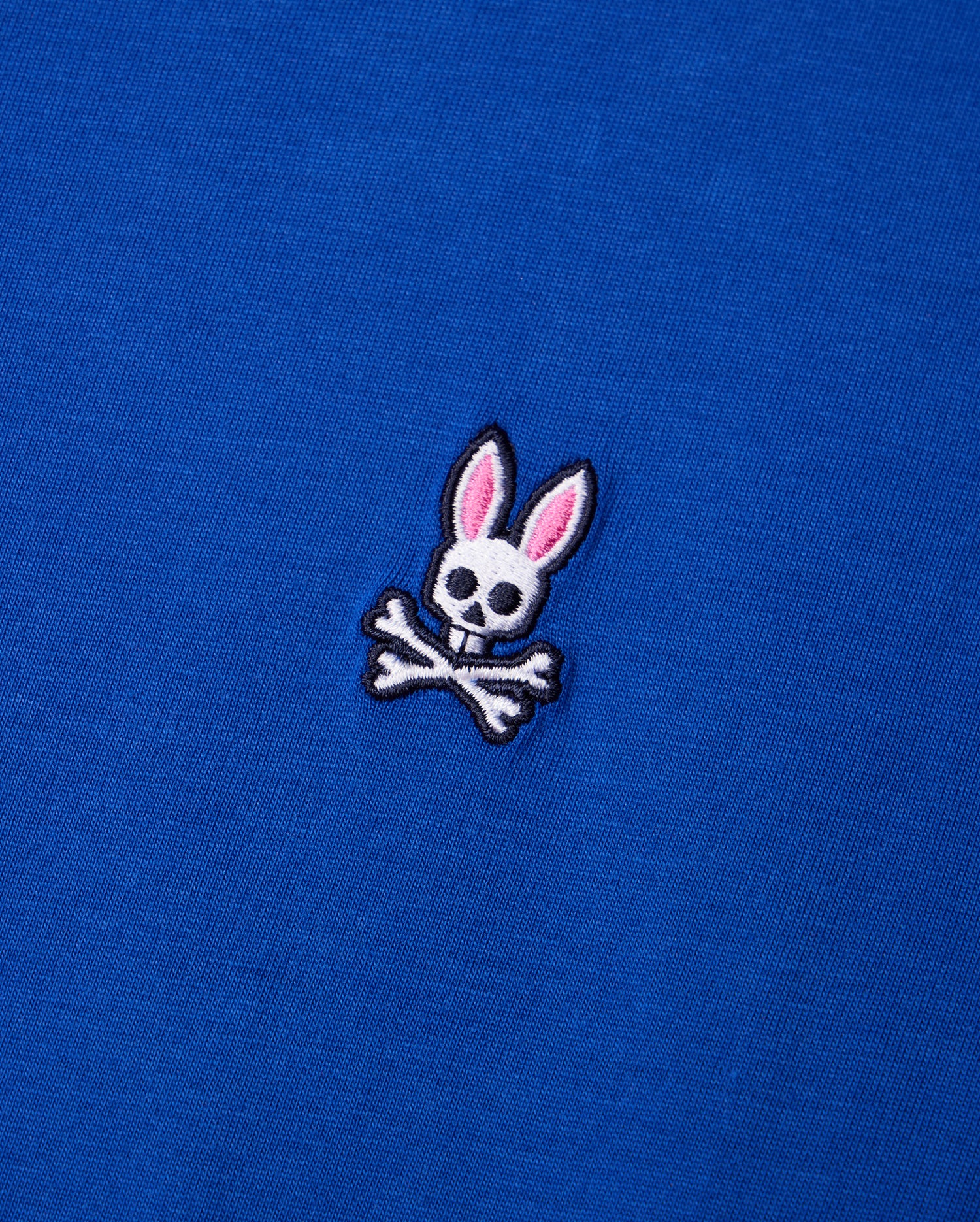 Crafted from luxurious Pima cotton, the Psycho Bunny MENS CLASSIC CREW NECK TEE - B6U014CRPC features a subtle embroidered logo of a rabbit skull with pink ears elegantly perched above crossed bones, creating a striking contrast against the blue fabric.