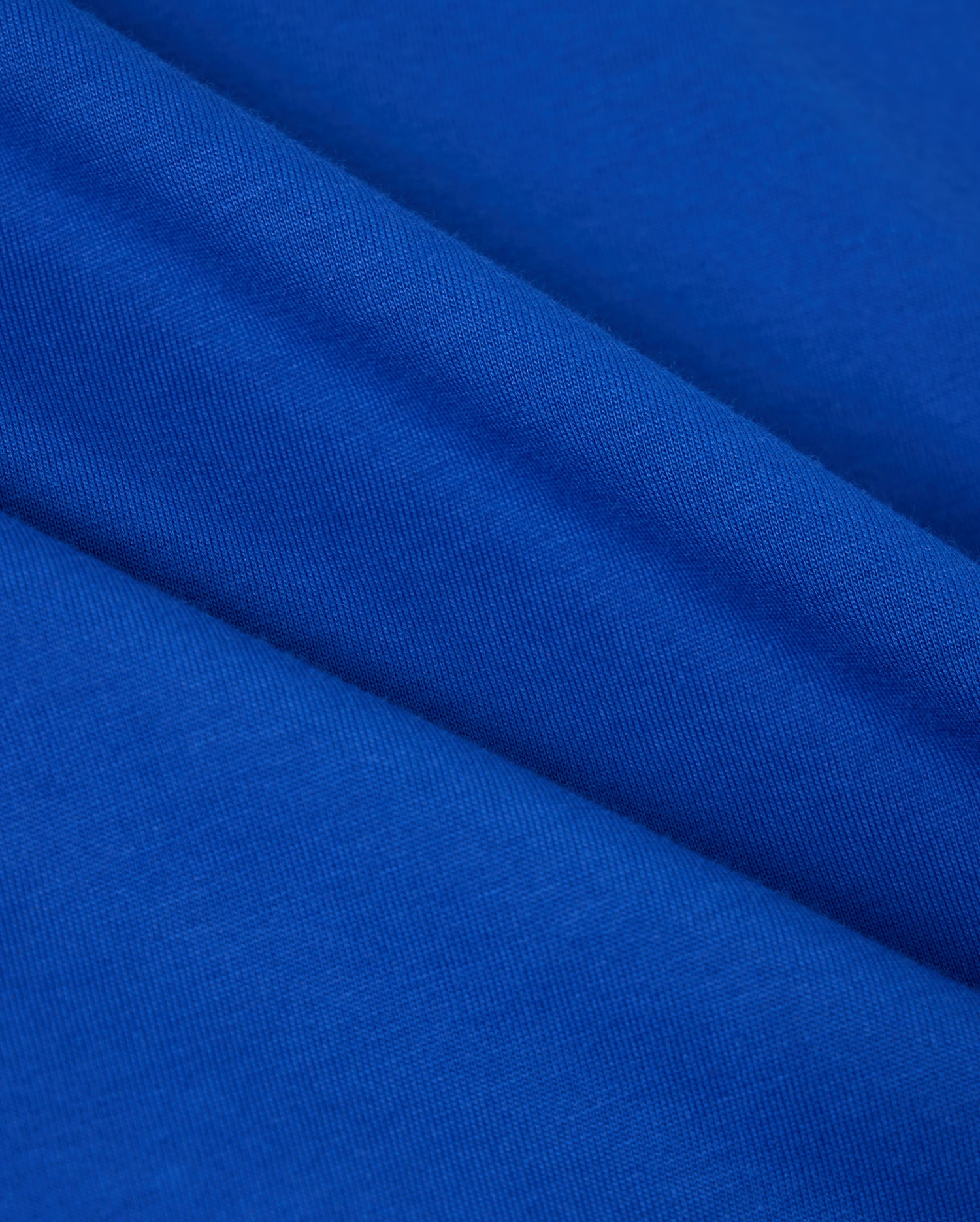 Close-up of vibrant blue Pima cotton with a smooth texture and diagonal folds. The material radiates a soft and lively appearance, highlighting the weave pattern—ideal for the Psycho Bunny Men's Classic Crew Neck Tee (B6U014CRPC) featuring an embroidered Bunny logo.