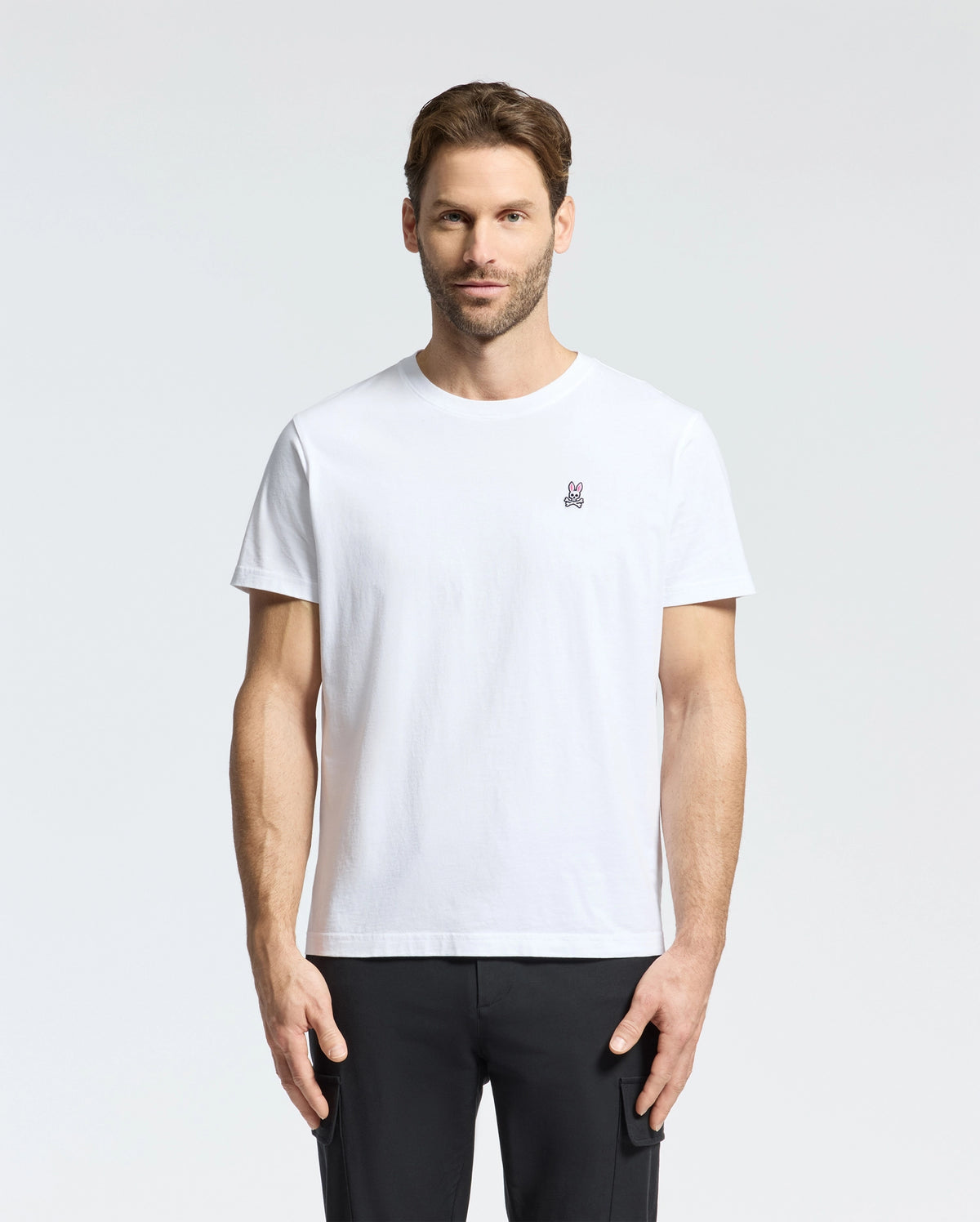 A person with short brown hair and a beard wears the Psycho Bunny MENS CLASSIC CREW NECK TEE - B6U014CRPC, made of 100% Pima cotton with an embroidered logo on the chest. They stand against a light gray backdrop, highlighting the comfy fit perfect for big and tall enthusiasts.