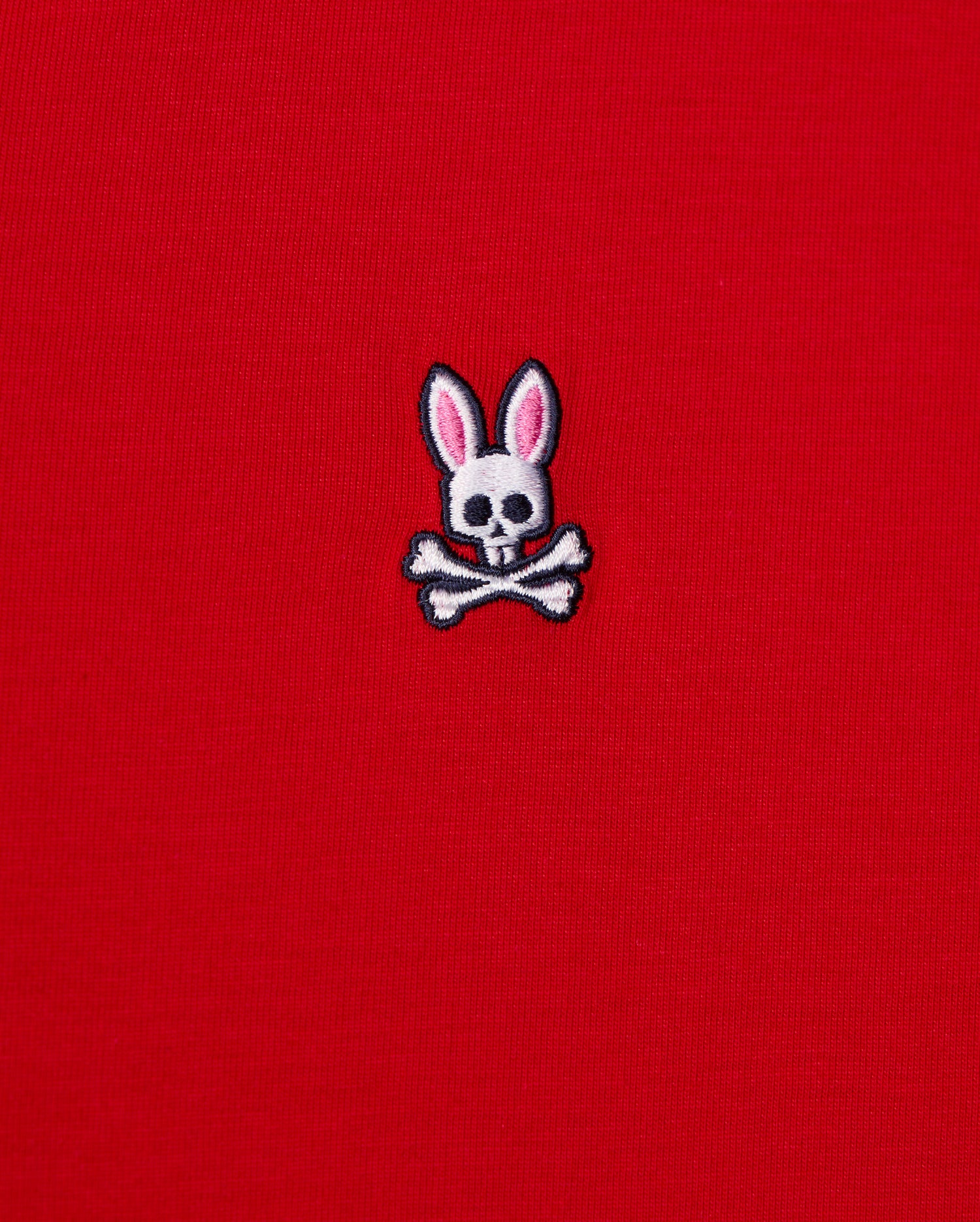 This men's v-neck tee, by Psycho Bunny, features a small emblem of a bunny skull with pink ears and crossbones embroidered on its bright red fabric. It's crafted from premium Pima cotton for exceptional quality. The product is named MENS CLASSIC V NECK TEE - B6U100CRPC.